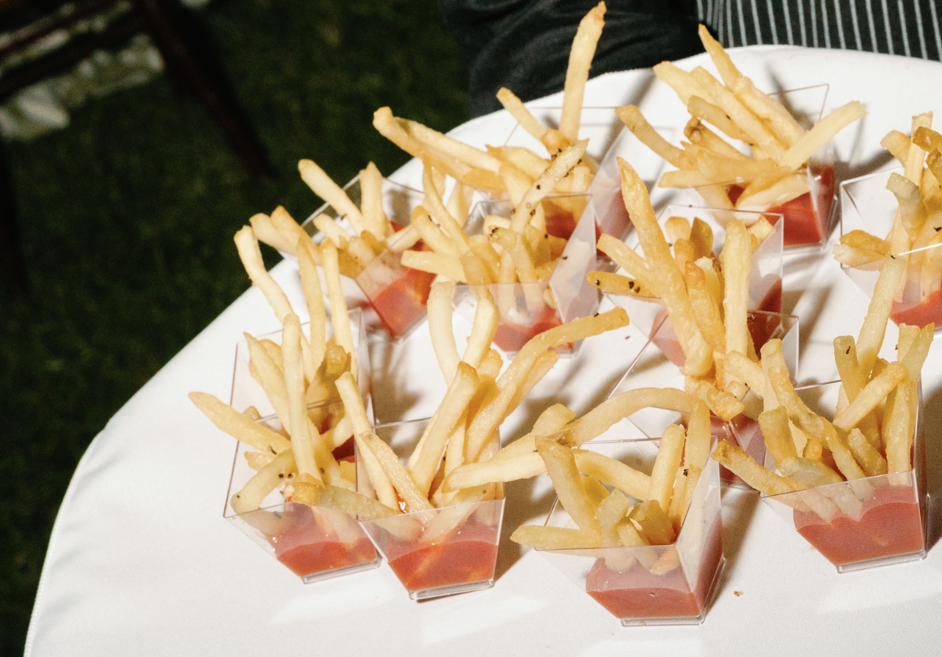 A tray holds several small clear cups, each filled with French fries and a serving of ketchup at the bottom, arranged on a white surface.A tray holds several small clear cups, each filled with French fries and a serving of ketchup at the bottom, arranged on a white surface.