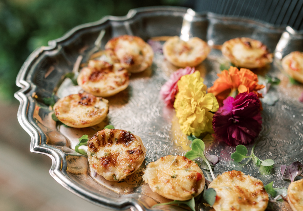 Mini tomato pie appetizers served on a silver platter with floral garnish.