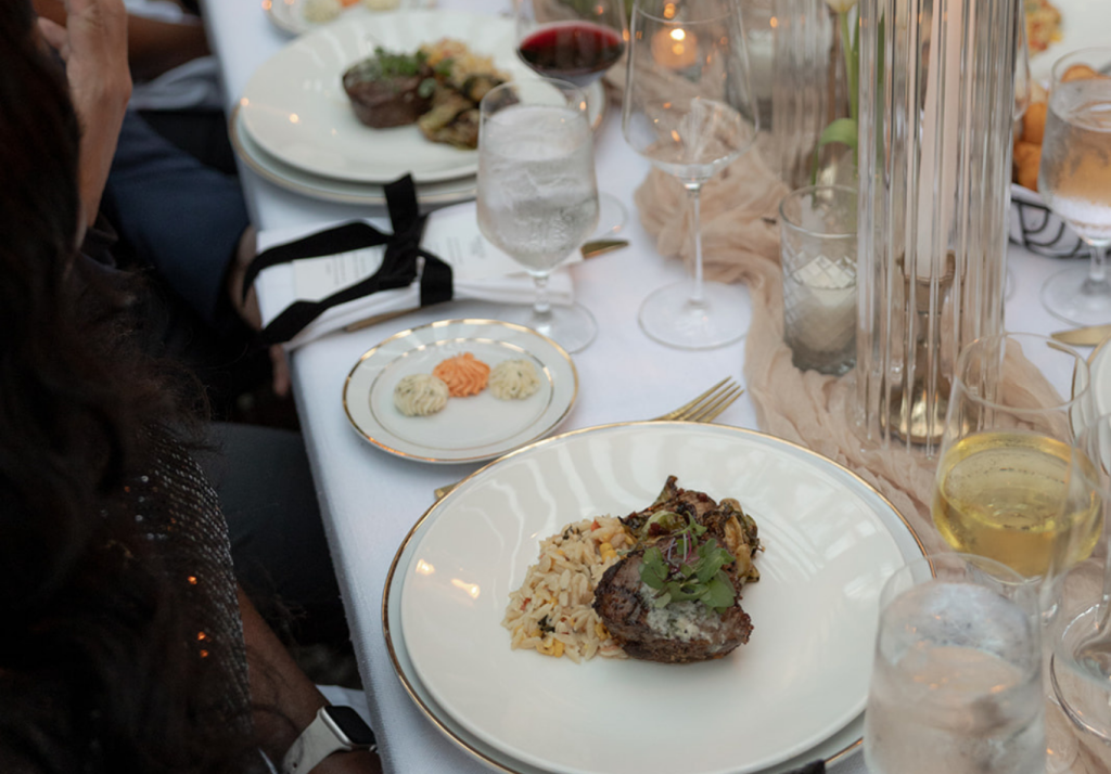 Plated filet of beef with rice served at an elegant rehearsal dinner with gold-rimmed dinnerware and candlelit tablescape.
