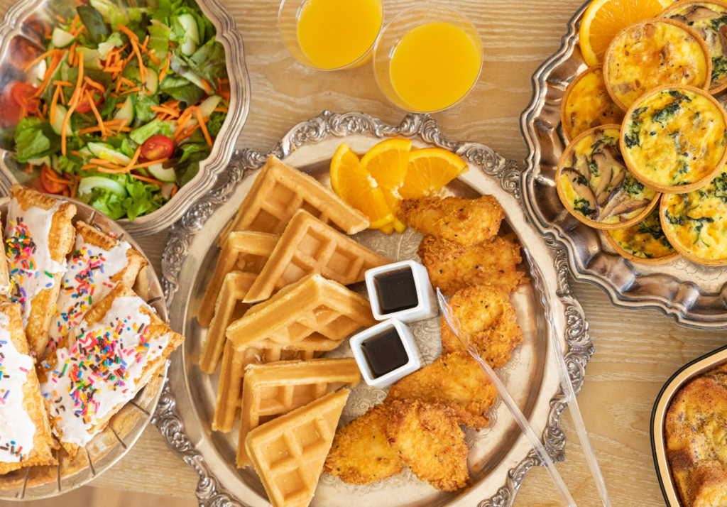 Wedding farewell brunch spread featuring chicken and waffles, mini quiches, fresh salad, pastries and orange juice.